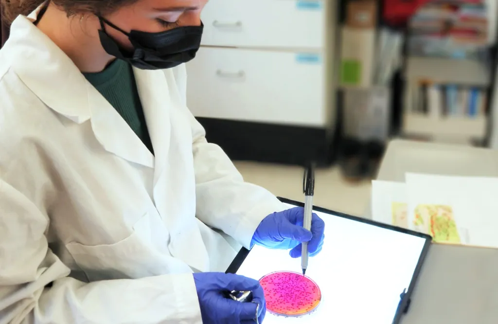 A student in a white lab coat marks a petri dish with a permanent marker