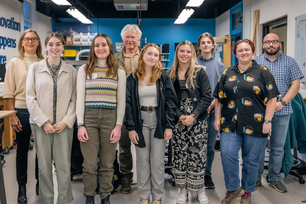A group of seven students and two faculty members pose in the Makerspace