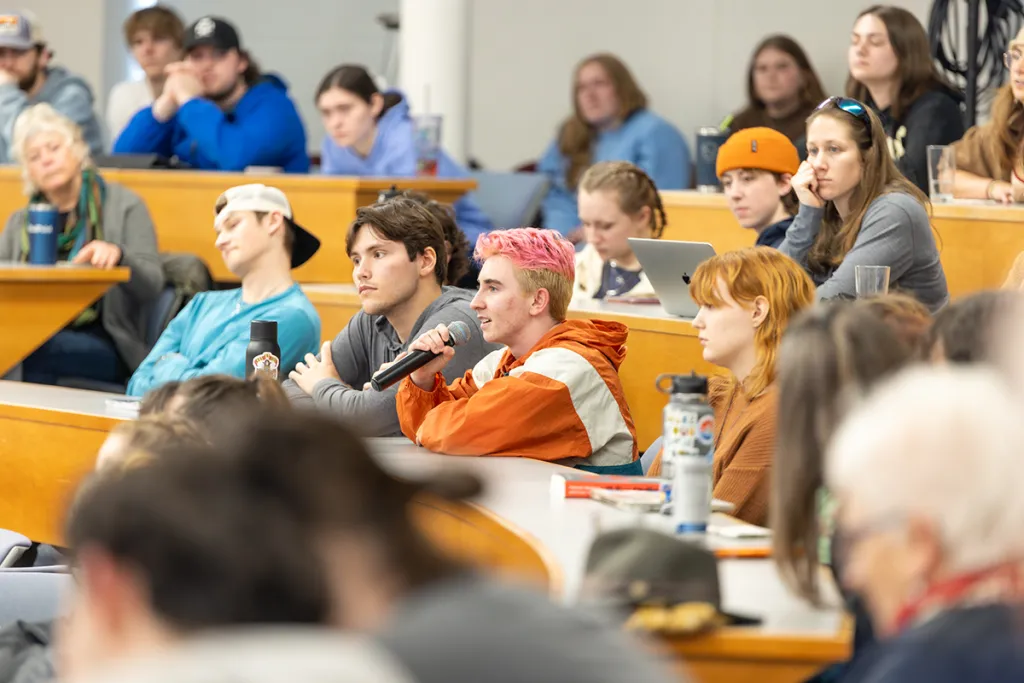 A student speaks into a mic from a crowd in a lecture hall