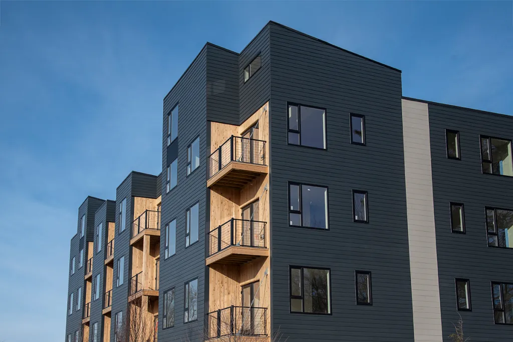 A blue-grey apartment building with wooden terraces