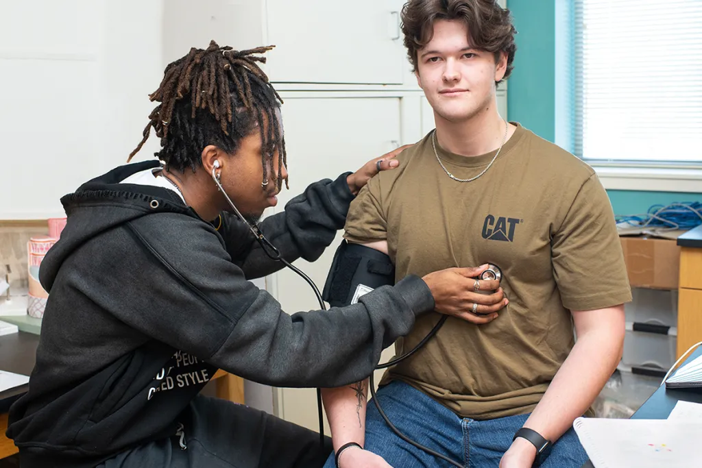 A student practices listening to the heart sounds of a fellow student using a stethoscope
