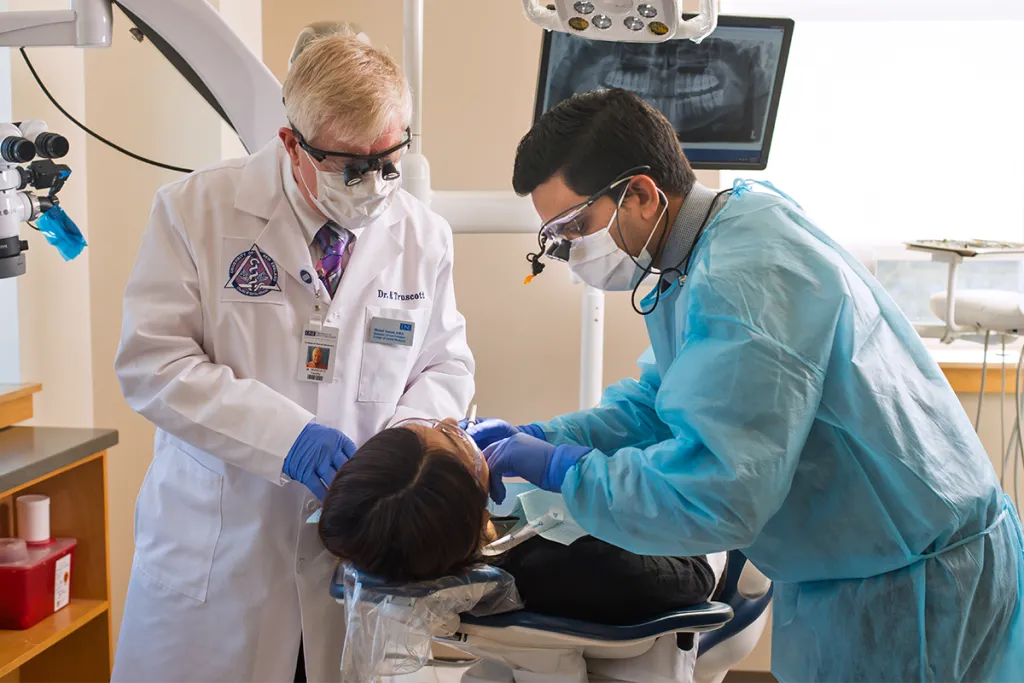 A C D M student looks at a patient's teeth while a professor reviews