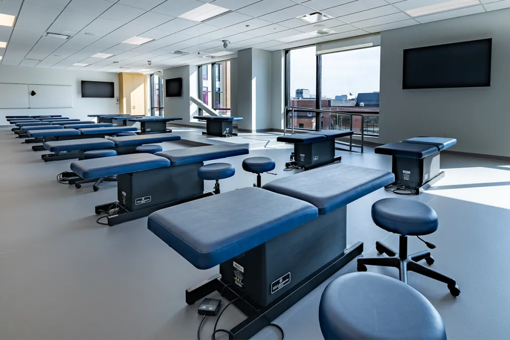 Rows of blue exam tables in a large room with large windows spanning one wall