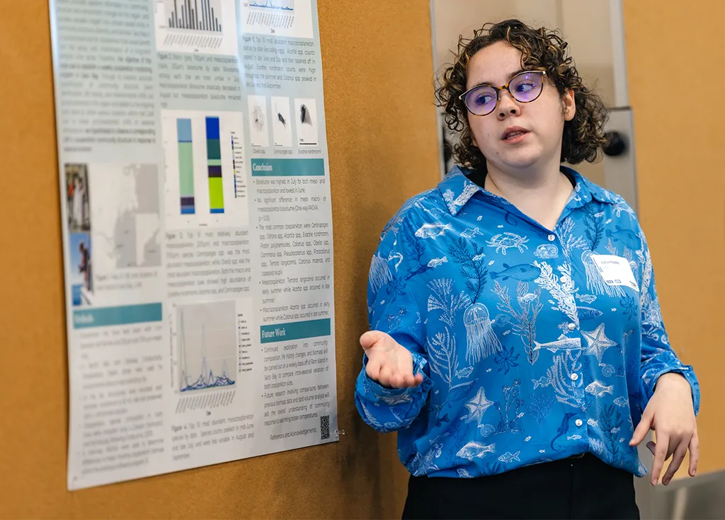 A U N E student explains their research poster on climate action at a workshop