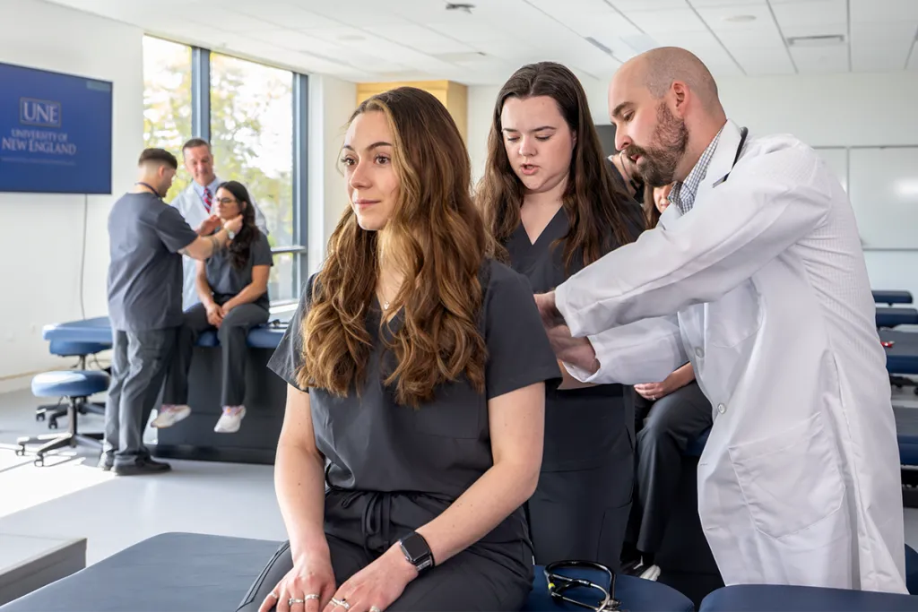 A physician assistant professor shows a P A student how to do a physical examination on another student