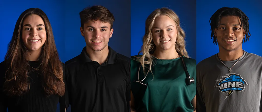 Four students smile for the camera in front of a dark blue background