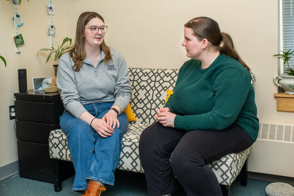 Two students sitting on a couch talk to each other