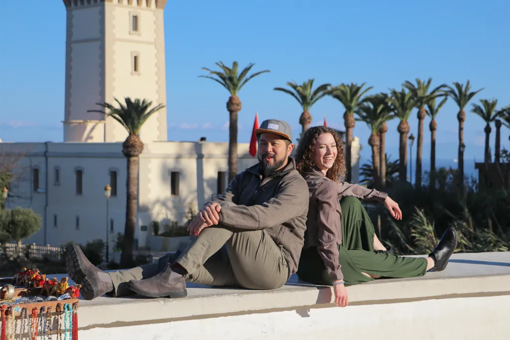 Two students pose together on a balcony in front of palm trees and a Moroccan tower