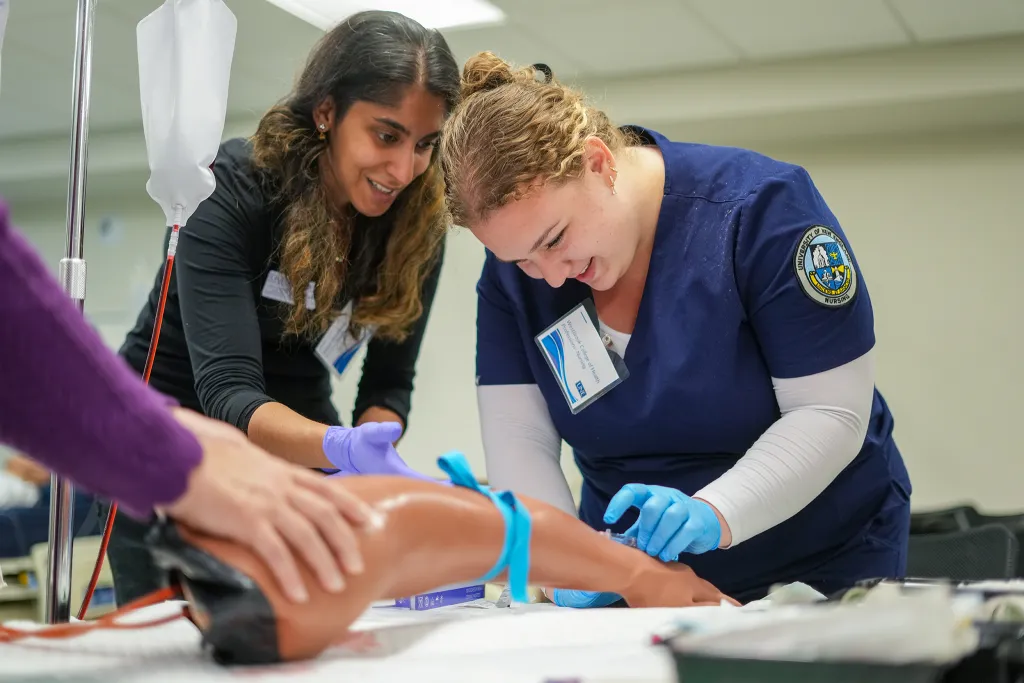A nursing student practices putting an I V into a sim lab patient arm