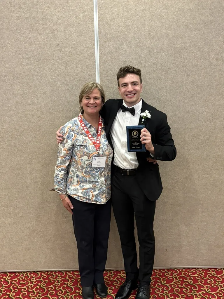 UNE student Aidan Curran holds an award and poses with UNE clinical professor Katie Hawke