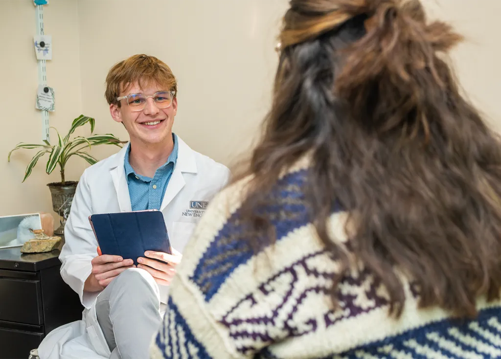A P M H N P student in a white coat speaks to a patient in an office setting
