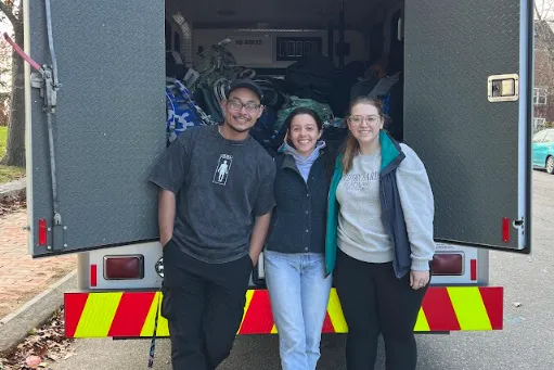 Three students stand at the back of an emergency response vehicle with fluorescent striping.