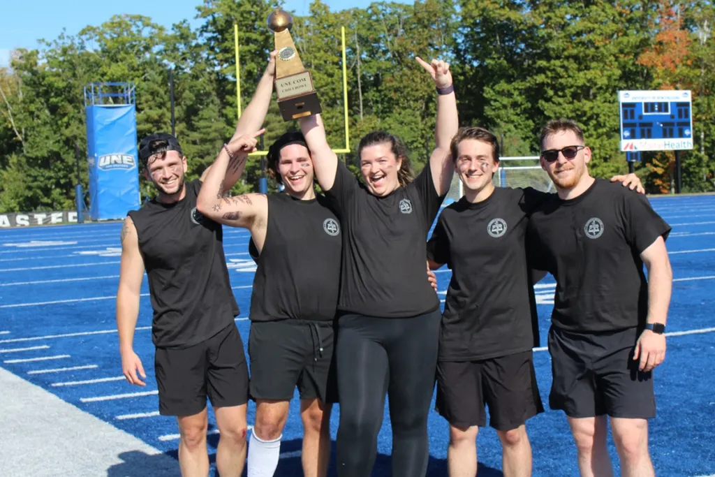 Six people in matching green shirts pose in front of a medical helicopter on a grassy field.