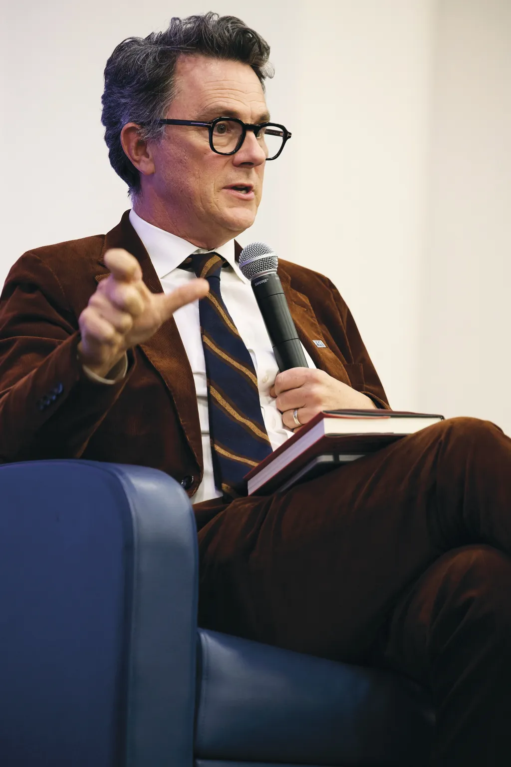 A panelist in a brown blazer gestures while speaking into a microphone during the President's Forum discussion on strongman presidency and democratic resilience