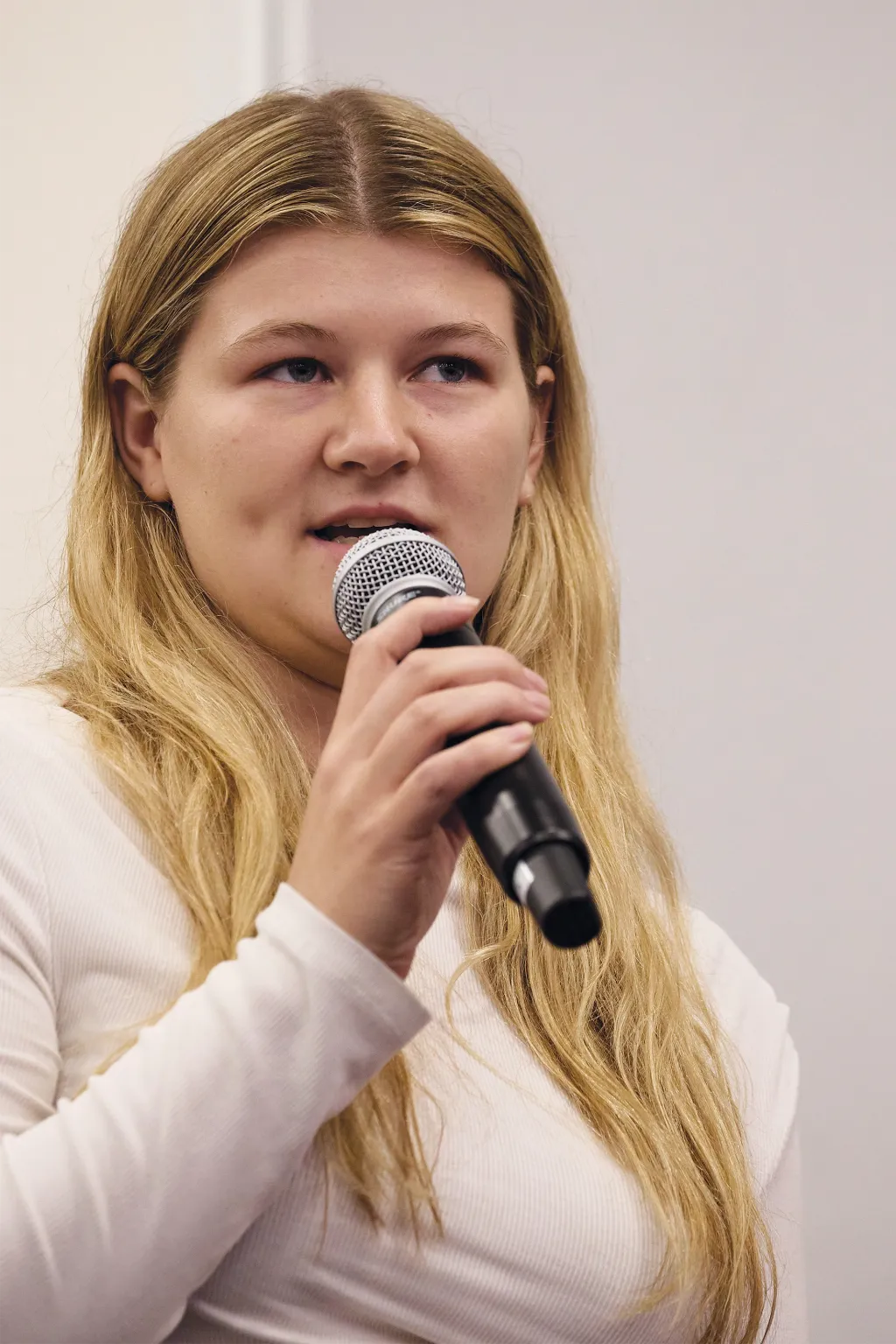 A student speaks into a microphone during the Q&A portion of the President's Forum, wearing a white collared shirt