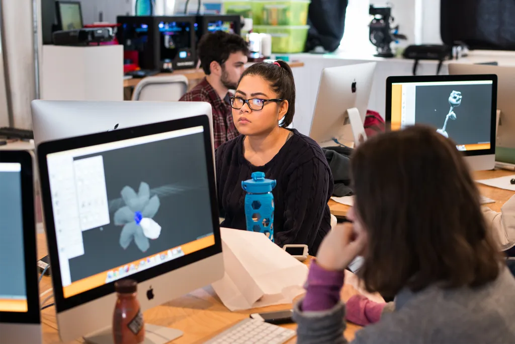 Students working on 3D animation and digital design projects at computer workstations in a collaborative classroom environment.