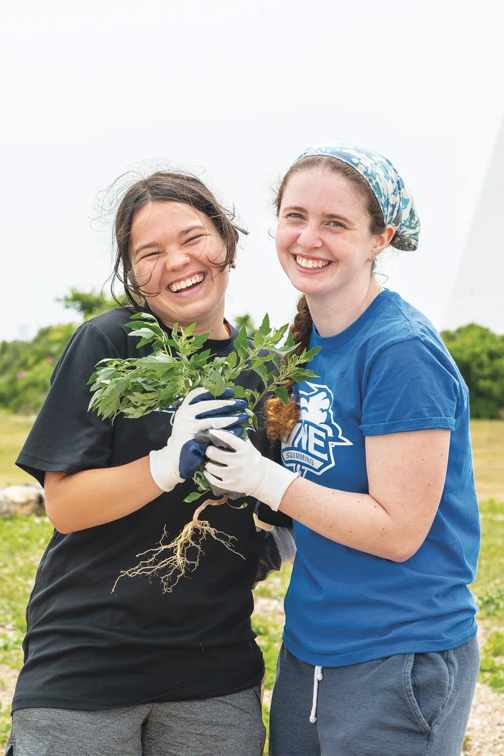 Annika Doeppers and another student smile while holding non-native plants during restoration work at Goat Island Light Station.