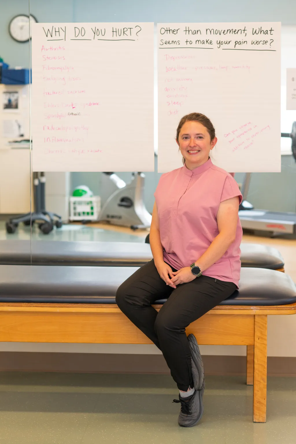 Olivia Franceschelli sits in the functional restoration program gym at Dartmouth Hitchcock Medical Center in front of whiteboards asking "Why do you hurt?" and discussing pain management strategies.