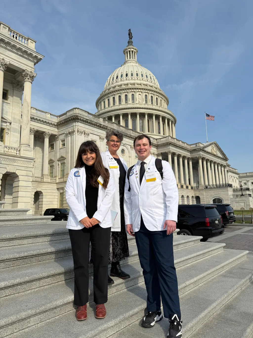 Two medical students and a faculty member pose in front of the U.S. Capitol building