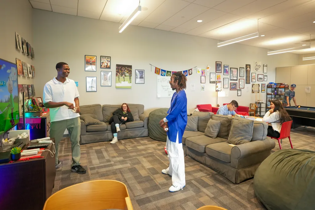 Students relax and play video games in U N E's cultural exchange lounge, decorated with flags, artwork, and photos from around the world.