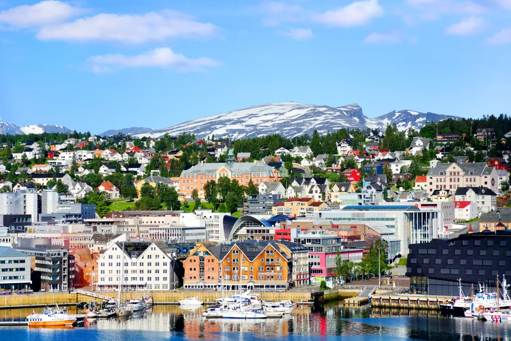 A summer view of Tromsø, Norway, showing the harbor and colorful waterfront buildings backed by snow-capped mountains.
