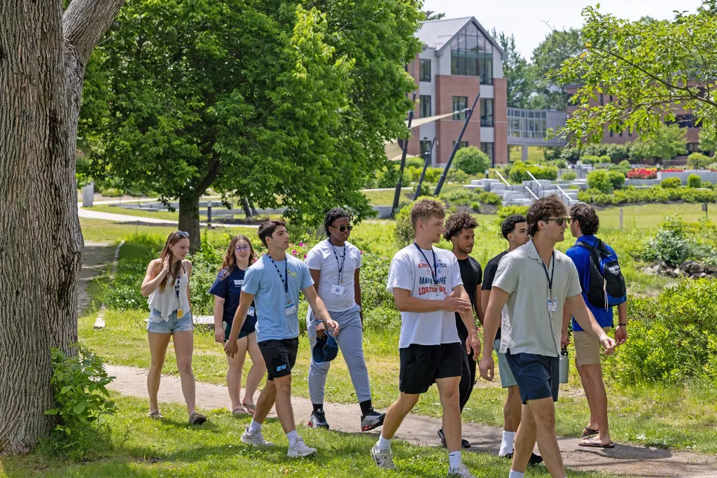 A group of incoming U N E students walk along a campus path near the Commons during orientation.