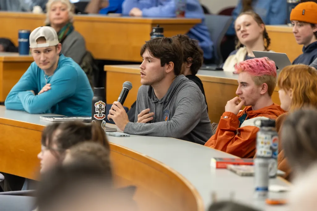 A U N E student asks a question with a microphone during a climate change lecture in a packed lecture hall.