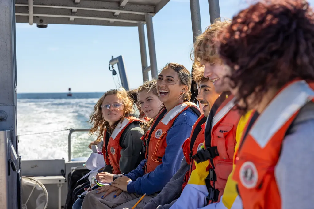 U N E students in life jackets laugh together aboard the research vessel Sakohki on a sunny day at sea.