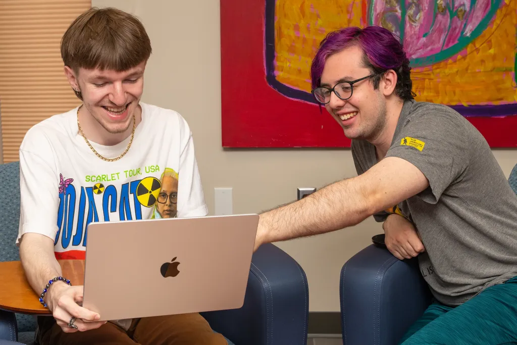 Two U N E students laugh together while looking at a laptop in Ketchum Library.
