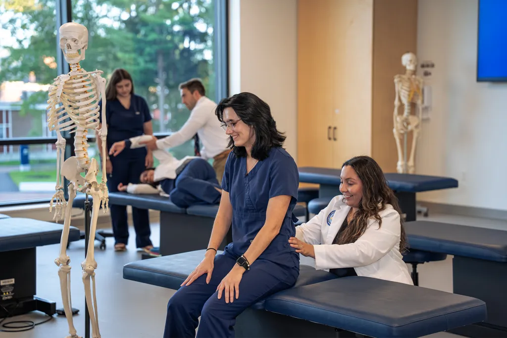 U N E College of Osteopathic Medicine students practice osteopathic manipulative techniques on classmates in a lab with skeleton models.