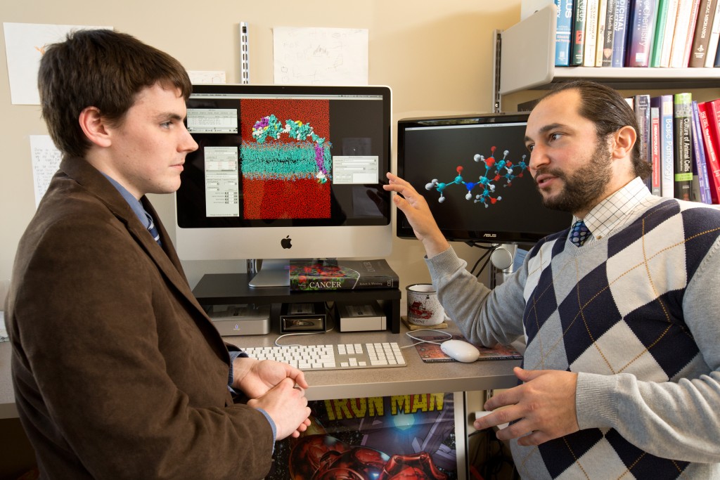 A male student sits with a professor discussing the molecular renderings on a computer screen