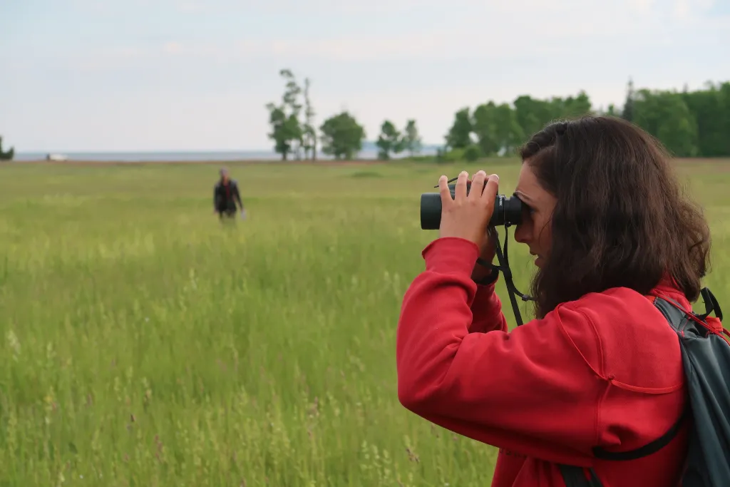 UNE student Olivia Scott uses binoculars to identify a previously banded bobolink at Shelburne Farms in Vermont