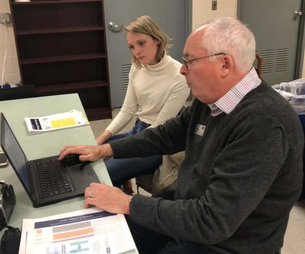 Tom Meuser explains how the Legacy Scholar Program works to Emma Simard, Maine Magazine associate editor