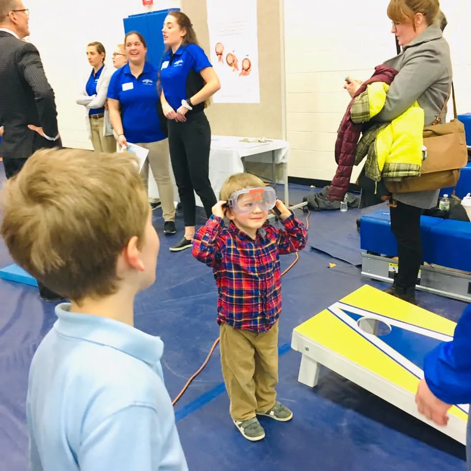 Jonah Cote tries on some goggles at UNE's Brain Fair, while President Herbert chats with some students