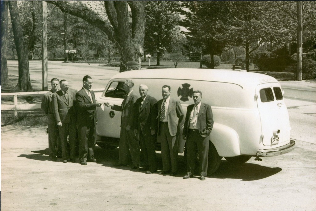 Historic image of a white ambulance with several men standing in front of it