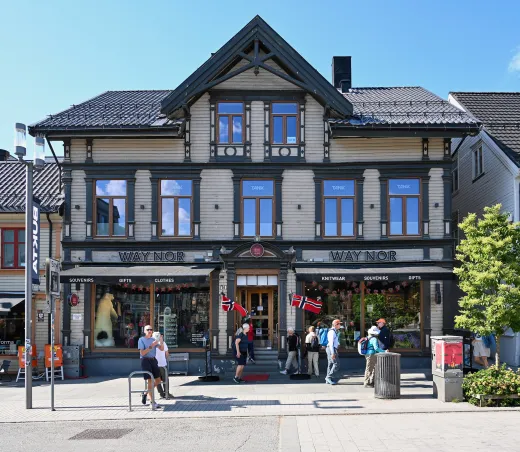 Pedestrians walk past a historic wooden storefront selling souvenirs and gifts in downtown Tromsø, Norway.