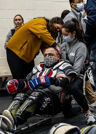 UNE physical therapy students fit a man for an adaptive hockey sled