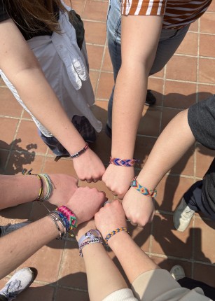 Students' hands come together with traditional bracelets on their wrists