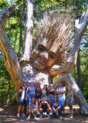 A group of U N E students stand in front of a giant troll installation at the Maine Botanical Gardens