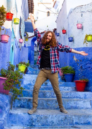 A student poses on an outdoor stairway amongst the blue-washed buildings of Chefchaouen, Morocco
