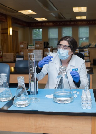 A pharmacy student examines beakers while making hand sanitizer