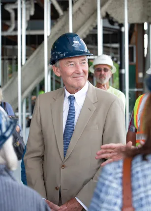 A man in a hard hat and a suit stands in front of the Health Sciences building construction