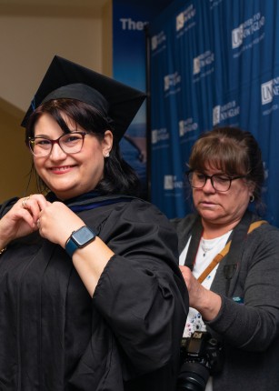 A faculty member help a student put on their gown at commencement