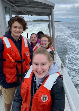 Students smile while wearing lifejackets on a U N E boat