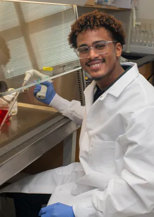 A student researcher smiles while holding lab equipment