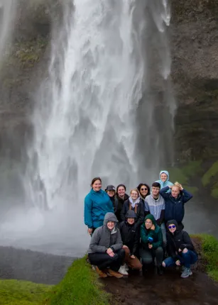 A group of U N E students pose together in front of a tall waterfall