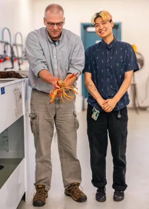 Markus Frederich holding a lobster standing next to Ruby Motulsky in the lab