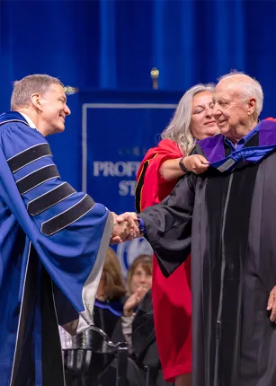 Gwendolyn Mahon gives Arthur P. Girard his sash while U N E president James Herbert shakes his hand