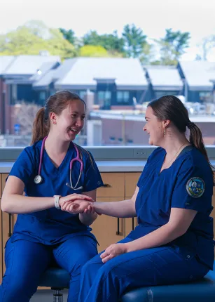 Two nursing students in dark blue U N E scrubs practice taking a pulse