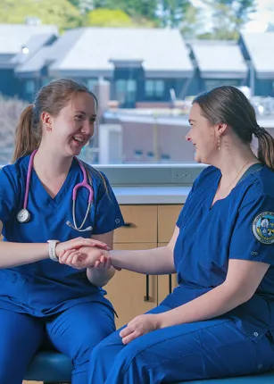 Two nursing students in dark blue U N E scrubs practice taking a pulse